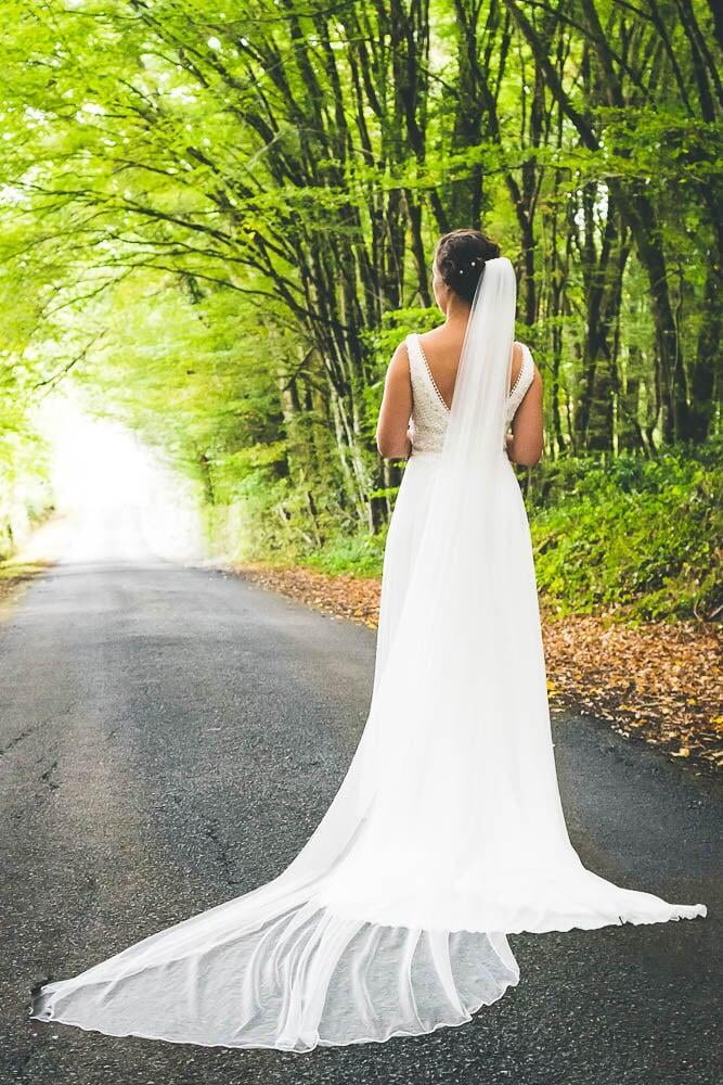 Femme mariée regarde au loins dans une foret avec grande robe de mariée blanche