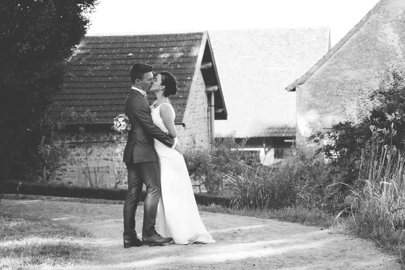 Mariés s'embrassent devant une ferme. 